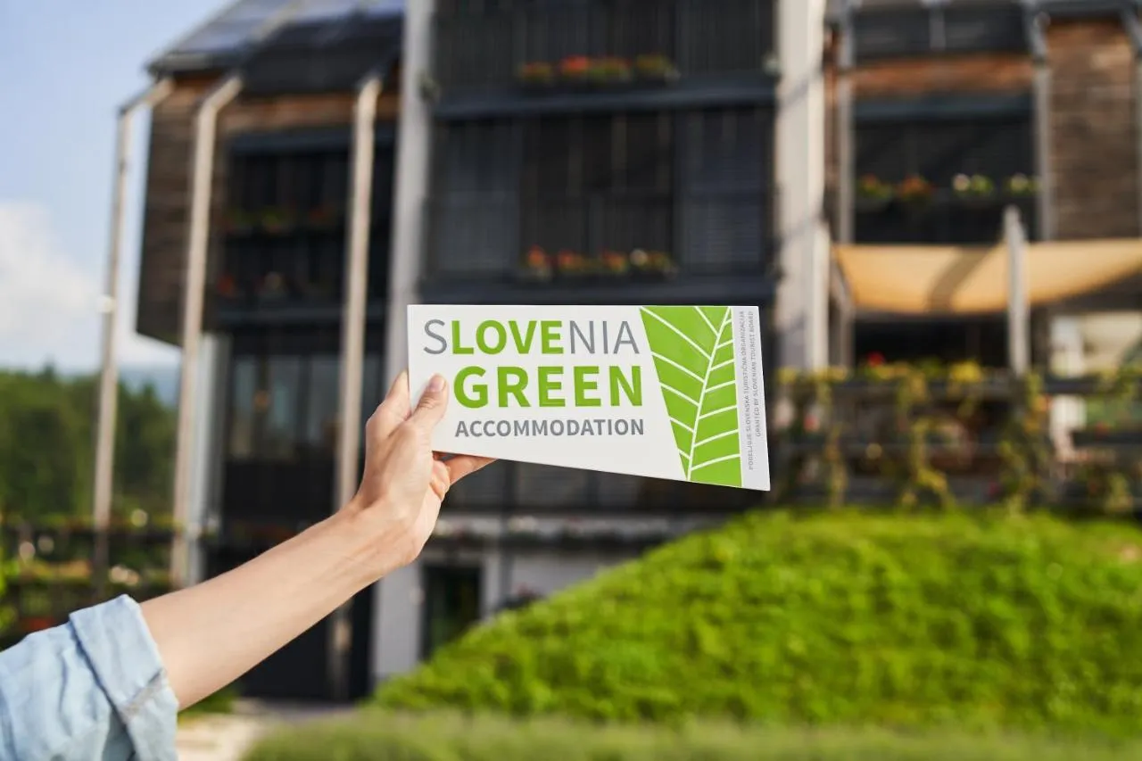 Znak Slovenia Green Accommodation pred hišo z zeleno streho